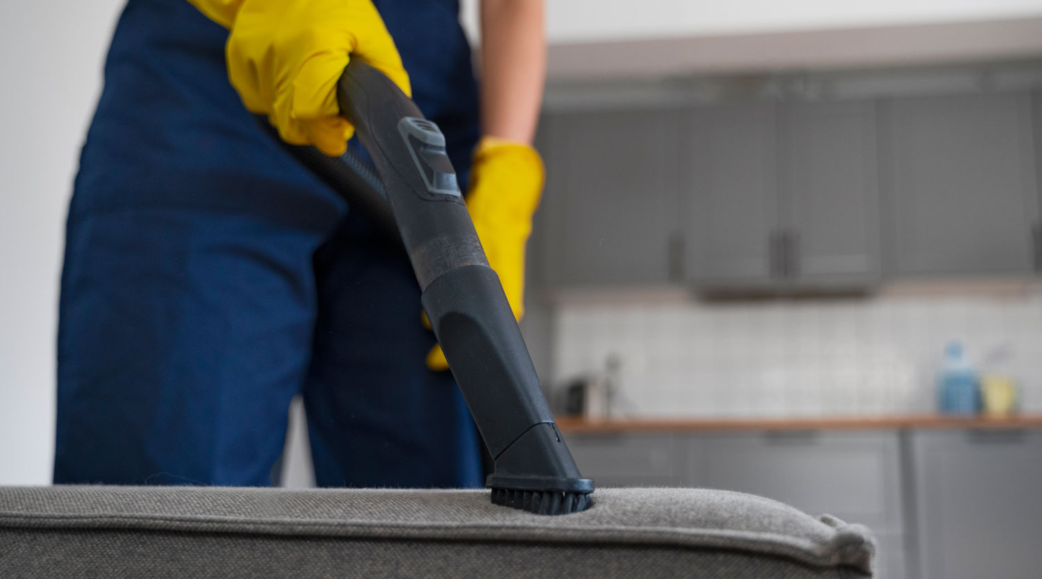 A Cleaner cleaning  sofa using vacuum cleaner